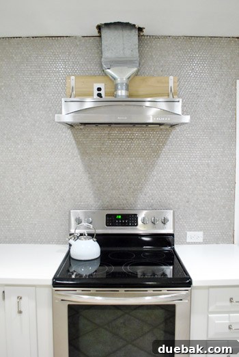 Close-up of installed range hood showing exposed pipe and wood