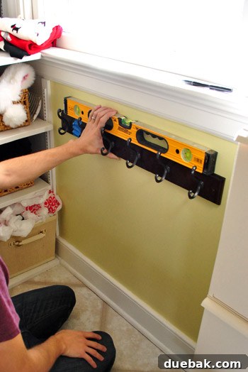 Streamline Your Laundry and Mudroom 2 Dark brown coat rack held up against a white wall in a laundry room for a size check.
