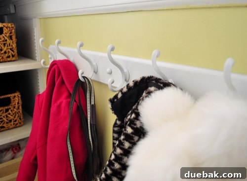 Streamline Your Laundry and Mudroom 5 Children's coats, hats, and a dog leash neatly hanging on the newly installed white coat rack in a laundry room.