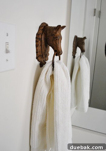 Vintage iron horse head wall hanging with a white hand towel draped through its ring, in a white bathroom.