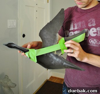 Person holding a vintage goose wall hanging with painter's tape applied to the back, marking the hanging points.