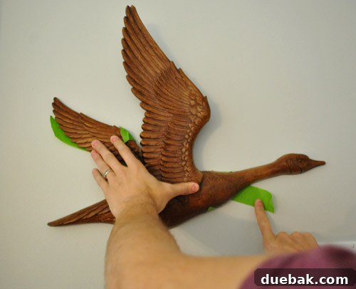 A person pressing the back of a vintage goose wall hanging against a wall, transferring the tape template.