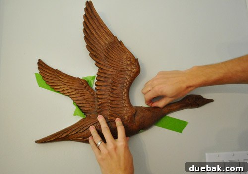 Close-up of hands firmly pressing painter's tape onto the wall where the goose art was positioned.