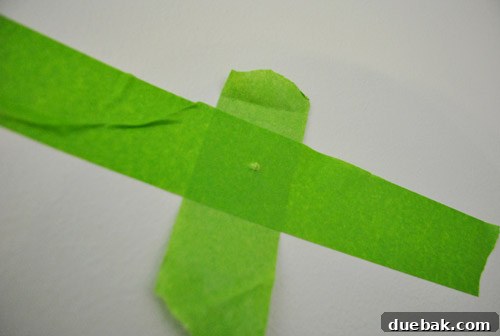 Close-up of the painter's tape template on the wall, clearly showing the marked spots for nail insertion.