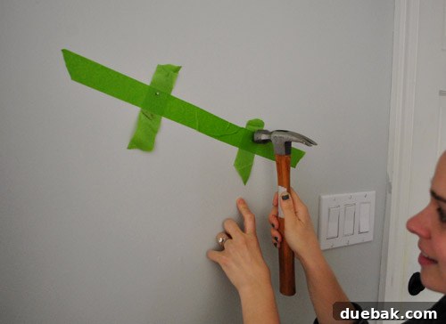 Person hammering nails into the wall at the marked spots from the painter's tape template.