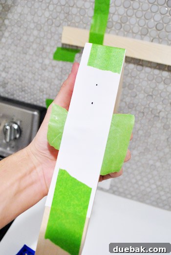 A paper template taped to a metal shelf bracket, with holes punched at the mounting points.
