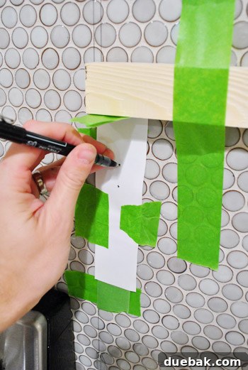 Close-up of the paper template on the tiled wall, showing the marked drilling points.