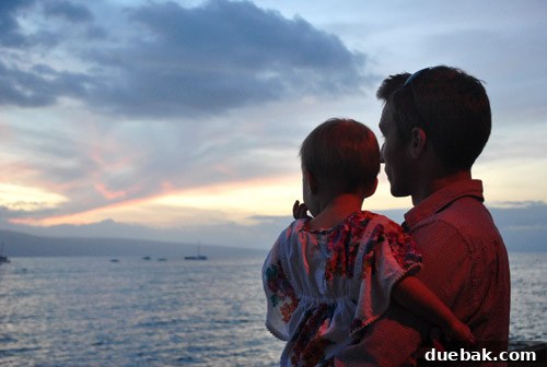 A family silhouette stands on a beach, watching a magnificent sunset over the Pacific Ocean in Lahaina.