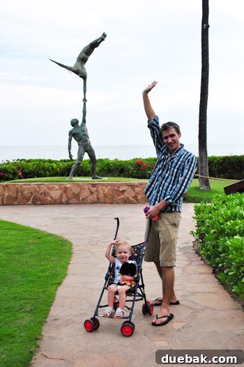 Clara raises her hand happily while on an oceanfront walk, enjoying the resort grounds with her parents.