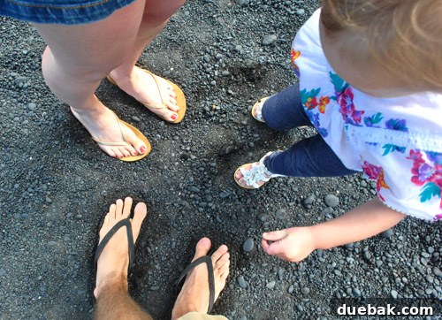 Clara stands by the ocean's edge on the black sand beach, mesmerized by the unique landscape.