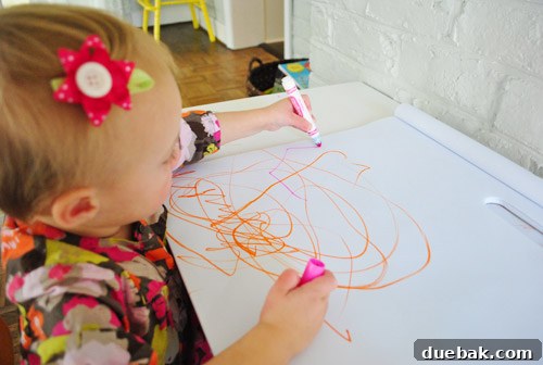 Clara holding a black marker, adding more scribbles to her vibrant artwork on the paper.