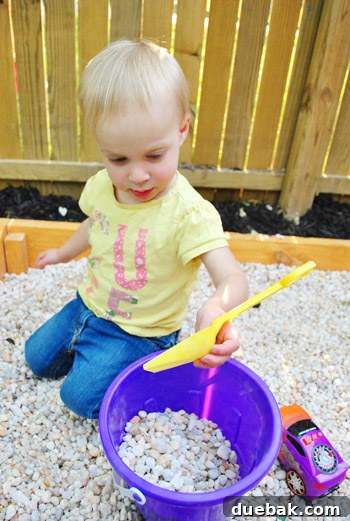Clara filling a toy truck with pea gravel