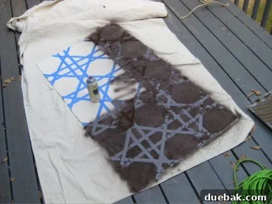 Close-up of a rug being spray painted with dark paint, highlighting the contrast between the taped and painted sections.