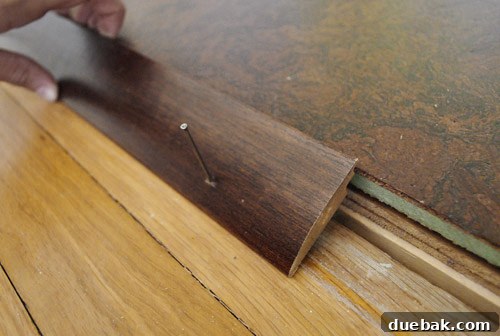 A transition piece carefully positioned in a doorway, showing its lip resting on the edge of the cork flooring.