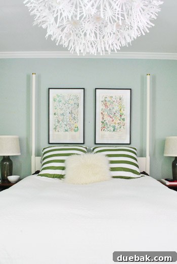 A wider shot of the bedroom showing the bed with the newly hung prints and the chandelier, highlighting the overall decor.