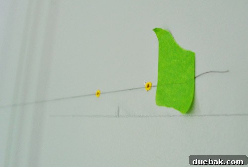 A close-up shot of a white sewing thread taped across a wall, used as a DIY level guide for hanging pictures.