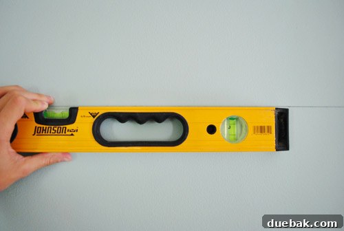 A spirit level placed against the stretched sewing thread on the wall, confirming its perfect levelness.