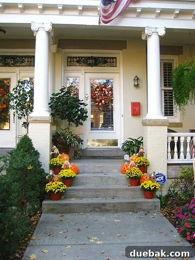 fanduringhalloween3 Elegant front porch with orange and white pumpkins, lush mums, and classic white columns on a historic home. A timeless autumn arrangement.