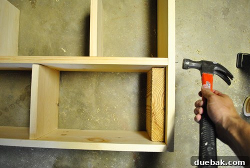 Assembling dollhouse side panels using glue and nails, with a scrap board for square corners