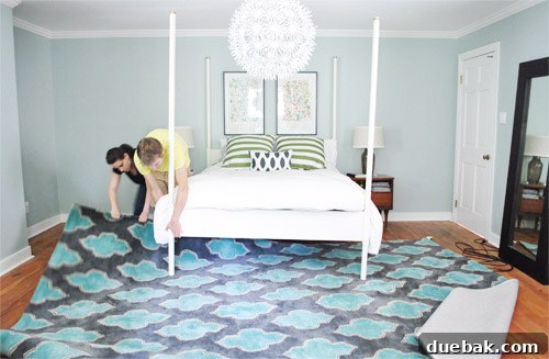 The new patterned rug being carefully positioned under the bed in the bedroom.