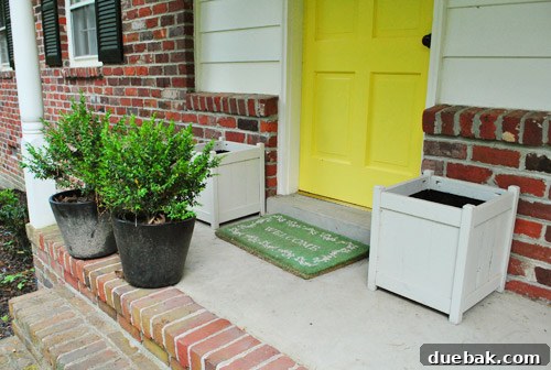Empty wooden planters flanking a front door, awaiting new plants, specifically boxwoods for curb appeal.