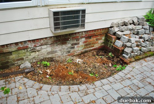 After relocating bushes, revealing a new empty and unlandscaped spot behind the patio, awaiting plants.