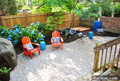 Bringing a Pop of Color to Our Side Patio with Red Adirondacks 21 Red Adirondack chairs on the patio with a wooden fence and Clara's rock box in the background