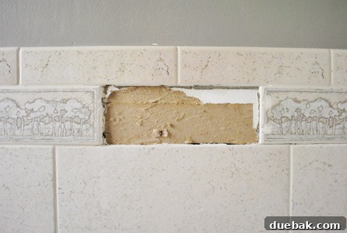 The first old tile successfully removed from the wall, revealing the exposed drywall underneath and adhesive residue
