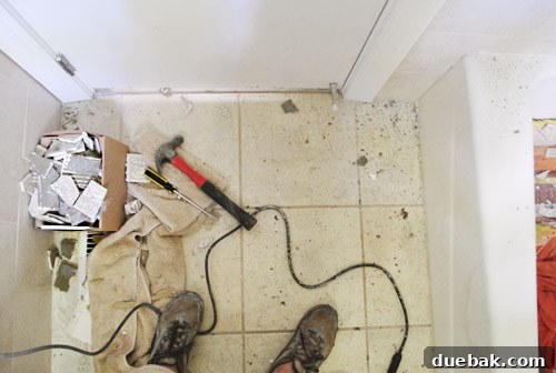 A large pile of removed tile, grout, and construction debris on the bathroom floor post-demolition