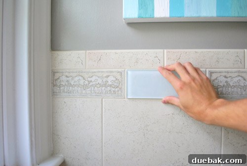 Comparing a clear glass subway tile against the existing beige tree-patterned border tile, showing a modern update