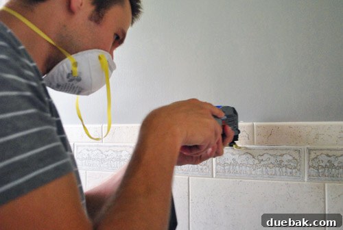 Close-up of using a Dremel Multi-Max tool to precisely remove old grout from between bathroom tiles