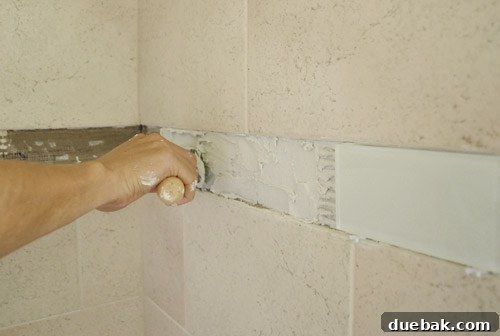 Bathroom wall with a section of new glass tiles installed and another section prepped with thinset