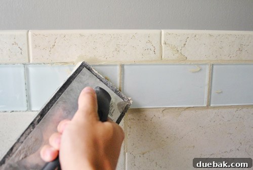 Cleaning excess grout from the surface of glass tiles with a damp sponge for a clean finish