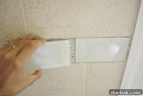 Continuing to install glass subway tiles around the bathroom walls