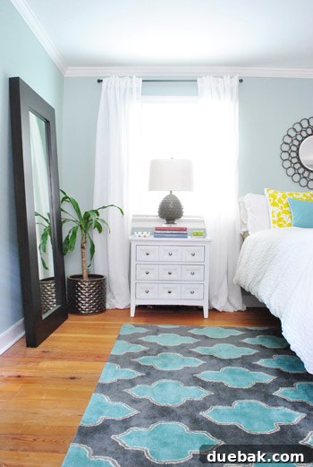 Bedroom details: A white nightstand by the window with a matching bedside lamp, contrasting with a wooden dresser.