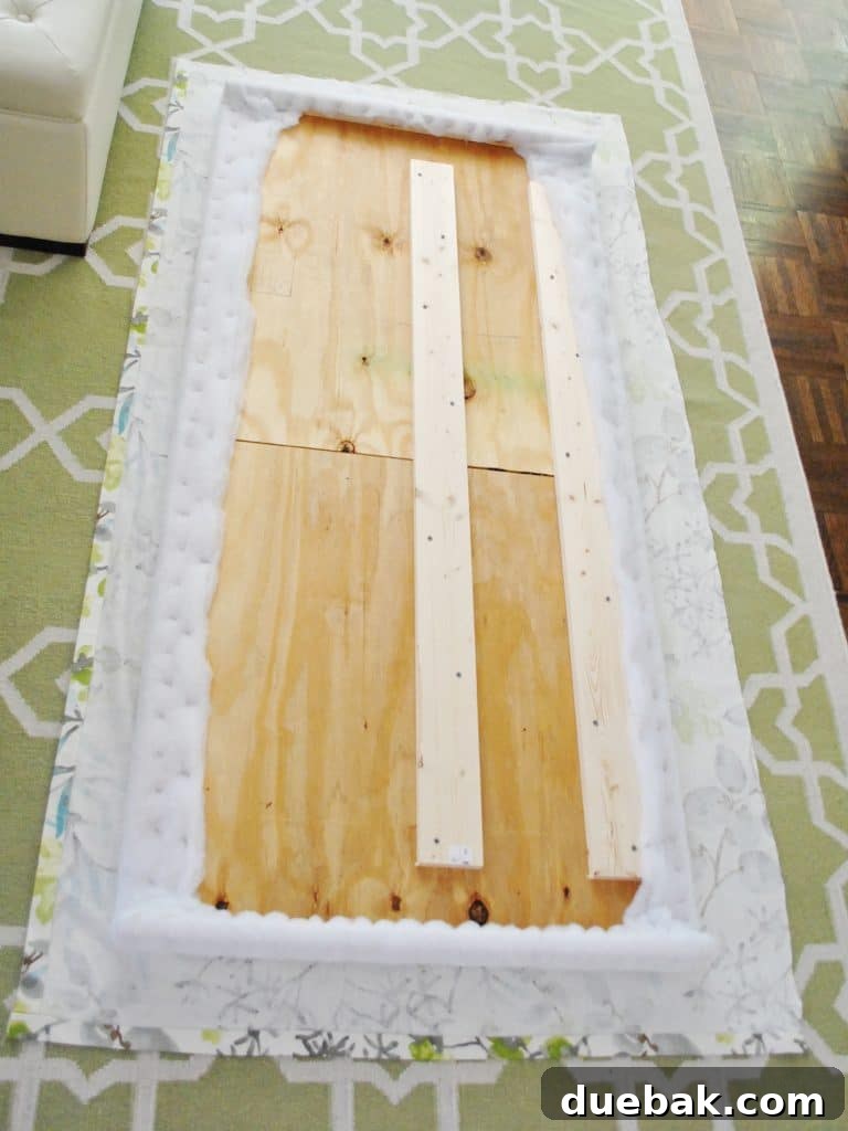 Fabric and headboard frame laid out on the floor to begin upholstery, with fabric positioned underneath
