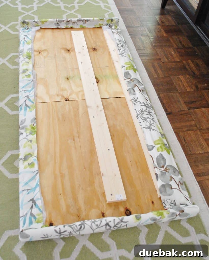 Fabric fully stapled along the backside of wooden headboard frame, demonstrating completion of fabric attachment