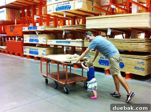 Clara, a young child, helping push a shopping cart at Home Depot with lumber