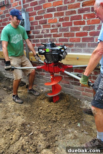 The auger bit shown deeply embedded in the ground, illustrating the progress of the footing excavation.