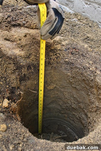 A man uses a manual post-hole digger to clear out remaining loose dirt from a deep deck footing.