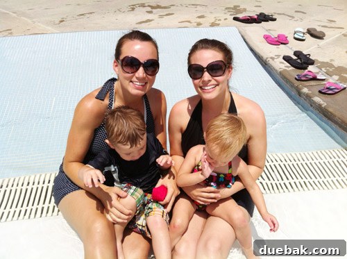 Two adults attempting to hold wiggly children for a photo at a pool