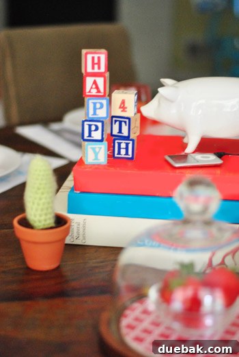 A whimsical kids' Fourth of July table setting with white dishware, crayons, blocks spelling 'Happy 4th', books, and playful treats.
