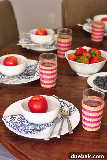 A casual Fourth of July table setting featuring white dishware, woven cups, red apples, and fresh strawberries and blueberries.