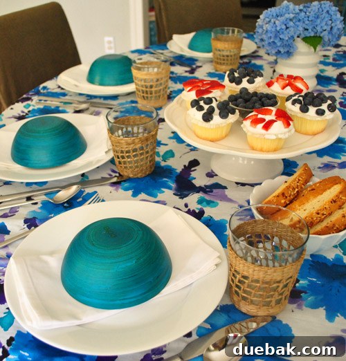 An elevated Fourth of July table setting featuring white dishware, blue bowls, a cake stand, and a fabric runner, with hydrangeas.