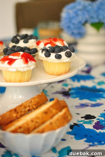 Close-up of store-bought cupcakes enhanced with fresh blueberries and sliced strawberries, embodying the 'lazy host' concept.