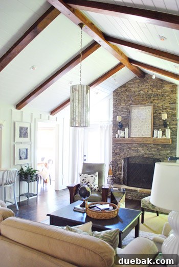 Vibrant Home Breakthrough 7 Lofted living room with faux board and batten walls, ceiling beams, and a large pendant light.