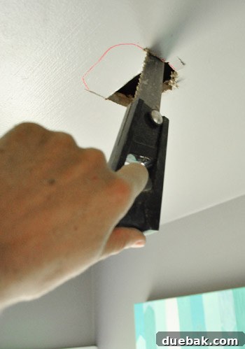 Cutting the final electrical box opening in the ceiling with a drywall saw