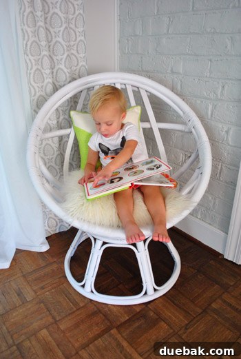 Clara reading an animal book while sitting in the egg chair, pointing at the bunny pillow.