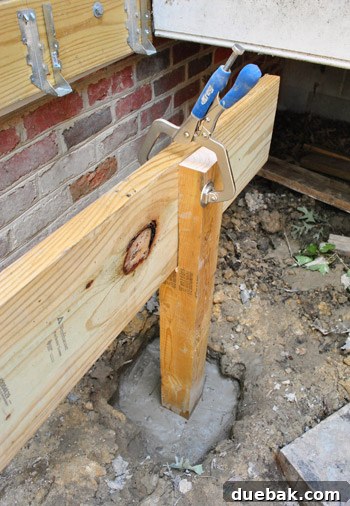 One end of a long girder clamped to a post, with the other end supported by a sawhorse
