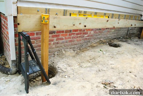 Man attempting to level a long girder board while marking a post
